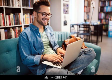 Felice studente che lavora su un portatile in biblioteca Foto Stock