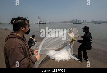 (200413) -- WUHAN, 13 aprile 2020 (Xinhua) -- Cheng Yishuang (2nd R) posa per le foto di matrimonio sulla riva del fiume Yangtze a Wuhan, provincia di Hubei della Cina centrale, 12 aprile 2020. Luo Jian e Cheng Yishuang avevano pianificato di scattare foto di matrimonio e di tenere la cerimonia di nozze a Wuhan dopo il Festival di primavera, che è caduto il 25 gennaio di quest'anno, ma il piano è stato inaspettatamente interrotto dall'epidemia COVID-19. Con l'annientamento dell'epidemia di coronavirus, Wuhan ha ripreso il servizio di registrazione del matrimonio per i cittadini dall'aprile 3. Anche le industrie correlate, come il noleggio di abiti e la fotografia di matrimonio, sono iniziate Foto Stock