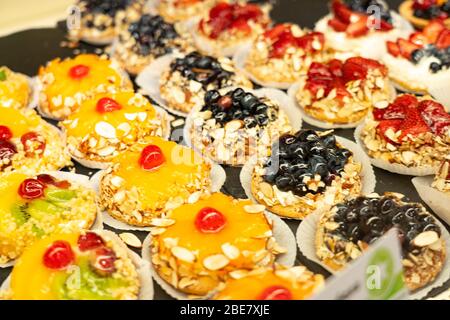 Torte e pasticcini in una vetrina. Pasticceria con varietà di ciambelle, crème brulee, torte con frutta e frutti di bosco. Foto Stock