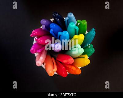 Vista dall'alto verso il basso delle penne da colorare che si spiralano in una pentola su uno sfondo nero Foto Stock