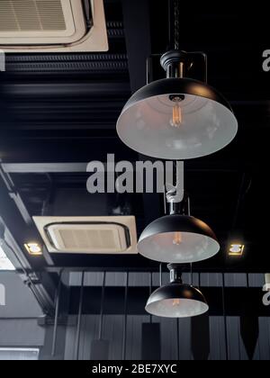 Tre luci da soffitto rotonde nere e aria condizionata di tipo a cassetta all'interno dello stile loft del cafe, stile verticale. Foto Stock