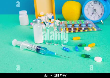 Siringa con flaconcini di vetro e farmaci pillole farmaco. Sullo sfondo si trova una scatola di legno e una mela gialla. Vista frontale Foto Stock