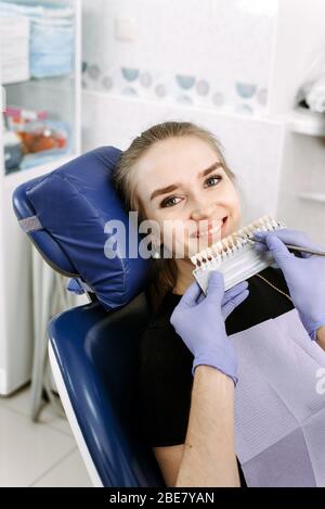 Il dentista seleziona il colore dello smalto dei denti per sbiancare una bella paziente ragazza. Scegliere il colore dei denti. Foto Stock