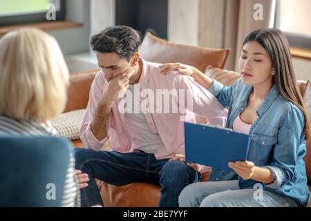 Sottolineato. Uomo alto dai capelli scuri seduto accanto alla sua ragazza guardando stressato Foto Stock