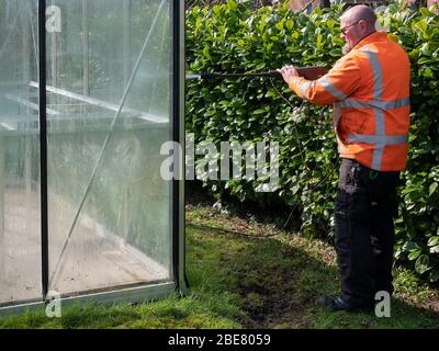 Addetto alle costruzioni che pulisce la sporcizia con pulitore ad alta pressione da una serra di vetro Foto Stock