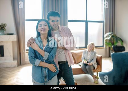 Buona coppia. Uomo alto dai capelli scuri che abbruta la sua ragazza dalle spalle e che guarda felice Foto Stock