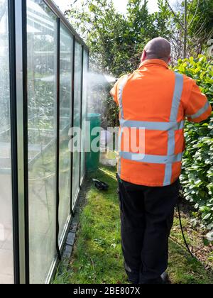 Addetto alle costruzioni che pulisce la sporcizia con pulitore ad alta pressione da una serra di vetro. Foto Stock