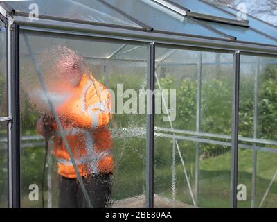 Addetto alle costruzioni che pulisce la sporcizia con pulitore ad alta pressione da una serra di vetro. Foto Stock