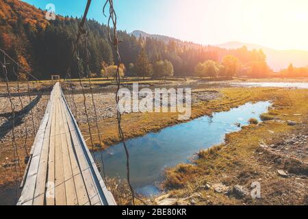 Ponte sospeso in legno sul fiume di montagna Foto Stock