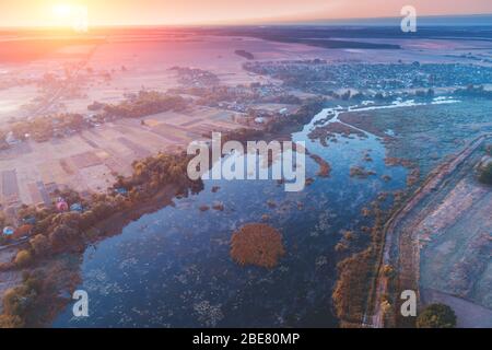Magico tramonto in campagna. Paesaggio rurale in serata. Vista aerea del fiume, campi e villaggio Foto Stock