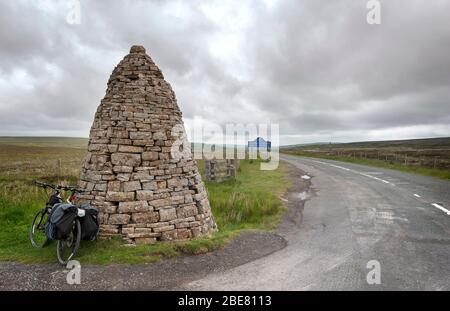 La bici da turismo si appoggia contro un grande barcaiolo di pietra, o currick, a Shorngate Cross al confine di Northumberland e della contea Durham, Regno Unito Foto Stock