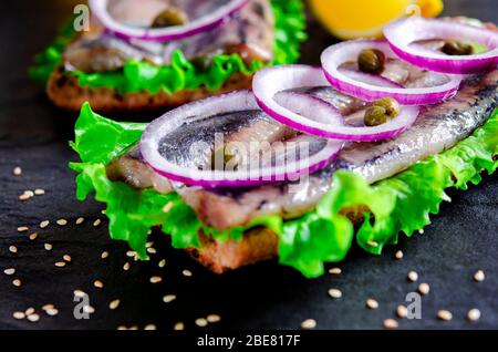 Panino con le aringhe salate, il burro e la cipolla rossa sul vecchio rustico tagliere. Messa a fuoco selettiva Foto Stock