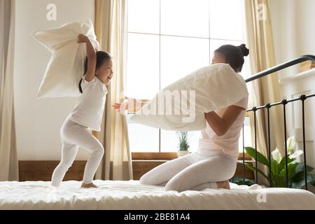 In camera da letto lotta con cuscini piccola figlia asiatica e madre Foto Stock