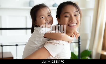 Piccola figlia asiatica piggybacks la sua vista della madre giovane closeup Foto Stock