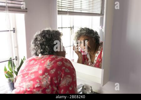 Una donna africana americana anziana che guarda la sua riflessione nello specchio e si prende cura di se stessa Foto Stock