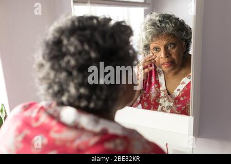 Una donna africana americana anziana che guarda la sua riflessione nello specchio e si prende cura di se stessa Foto Stock