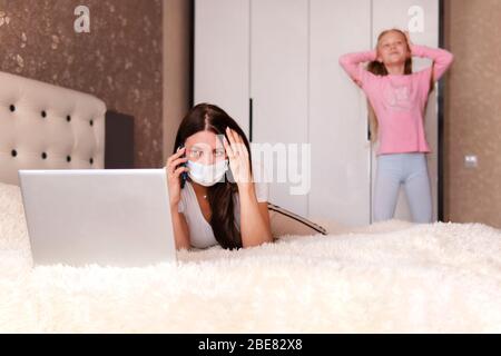 ragazza chiama sul suo smartphone. Lavoro remoto. Rimani a casa. Madre stanca che tiene la testa, cercando di lavorare a casa ma bambino che la disturba, camera da letto interiore. Foto Stock