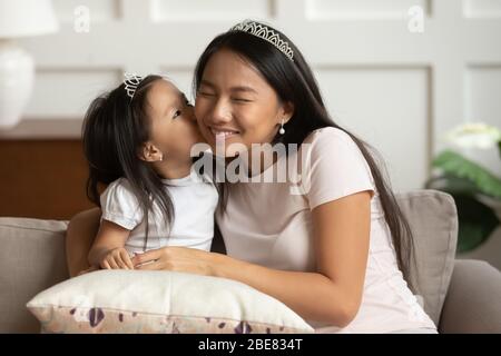 Piccola figlia asiatica bacia sulla giovane madre guancia Foto Stock