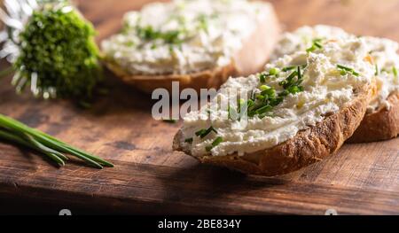 Primo piano di una spessa fetta di formaggio di pecora su fette di pane con erba cipollina tritata finemente sulla parte superiore. Foto Stock