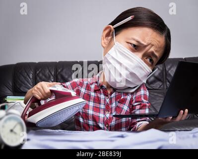 donna che lavora con parti di lavoro e di casa molto occupate, stirare i panni, parlare al telefono e lavorare con il computer portatile durante l'isolamento per evitare la sprea Foto Stock