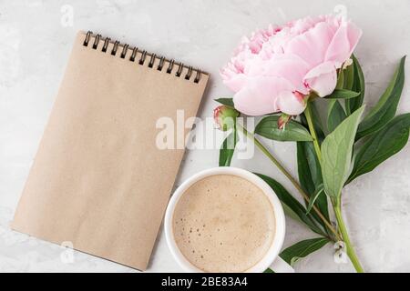 Taccuino di carta bianca, tazza di caffè e fiore di peonia rosa su tavolo di cemento. Stile nuziale. Disposizione piatta. Mock up. Vista superiore con spazio per copia Foto Stock