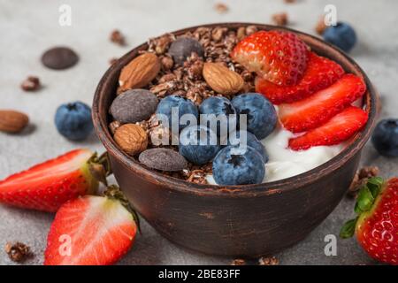 ciotola di cioccolato all'avena con yogurt, mirtilli freschi, fragole e noci su sfondo grigio per una colazione sana. primo piano Foto Stock