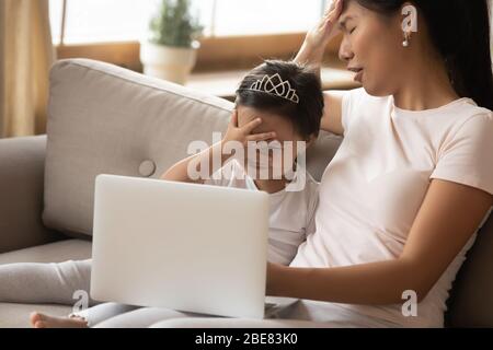 La famiglia asiatica che guarda i cartoni animati sul laptop facendo il facepalm è imbarazzante Foto Stock