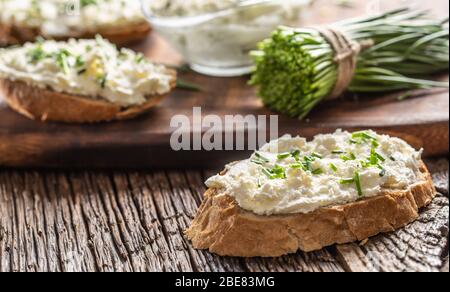 Fette di pane croccante con un formaggio spalmato e erba cipollina tagliata di fresco su un tagliere in legno d'epoca. Foto Stock