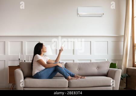Donna vietnamita che accende il condizionatore mentre riposano seduti al chiuso Foto Stock
