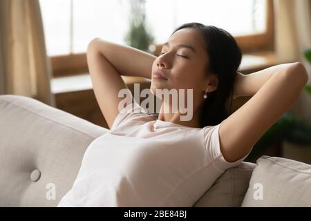 Donna asiatica ha messo le mani dietro la testa appoggiandosi sul divano primo piano Foto Stock