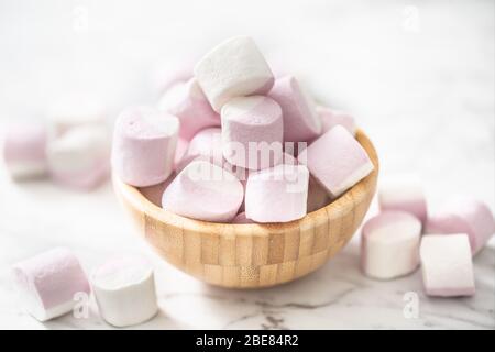 Ciotola in legno piena di marhsmallows con alcuni sparsi su una superficie di marmo in un ambiente leggero. Foto Stock