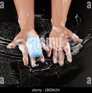 processo di lavaggio delle mani con sapone blu, parti del corpo in schiuma bianca su sfondo nero, vista dall'alto, concetto di igiene Foto Stock