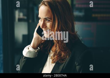 Donna d'affari che parla al telefono in ufficio. Donna caucasica sorridente in formalwear parlare sul telefono cellulare al lavoro. Foto Stock