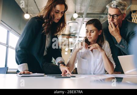 Donna d'affari che discute le nuove strategie con la sua squadra che siede intorno ad un tavolo. Gruppo di persone d'affari che si riunita per un nuovo progetto in carica. Foto Stock