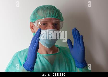 Infermiere maschio, con occhiali protettivi in plastica e maschera facciale, cappuccio, gonna, guanti, con dispositivi di protezione individuale per proteggere contro il virus co Foto Stock