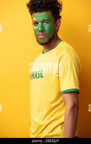 bel tifoso di football afro-americano con faccia dipinta come bandiera brasiliana su giallo Foto Stock