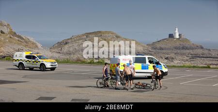 Nella foto: Un gruppo di giovani in bicicletta viene parlato da un poliziotto al parcheggio altrimenti deserta di Bracelet Bay vicino a Swansea, Galles, Regno Unito. Foto Stock