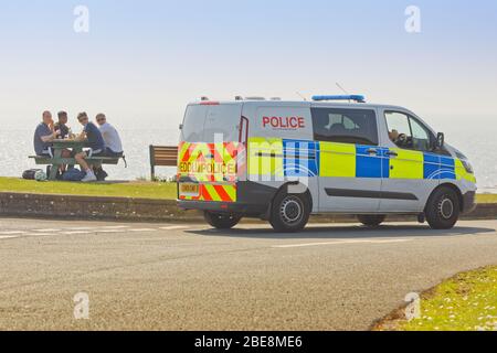 Nella foto: Un gruppo di quattro giovani viene parlato da un poliziotto mentre si ha un picnic a Bracelet Bay vicino Swansea, Galles, Regno Unito. Venerdì 10 aprile Foto Stock