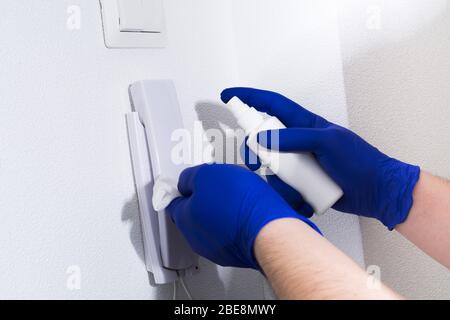 Uomo con guanti blu pulizia telefono porta con igienizzatore. Prevenzione di coronavirus e altri virus. Liquido spray uomo su tessuto Foto Stock