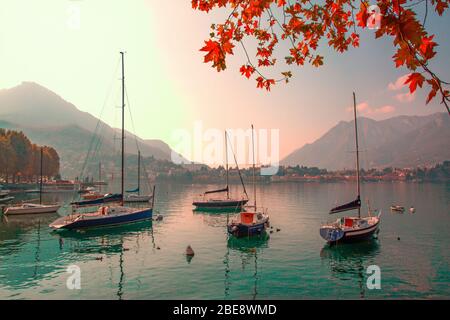 Lago di Como bellissimo paesaggio autunnale. Foglie rosse colorate, piccole barche e montagne sullo sfondo. Destinazione Italia. Foto Stock