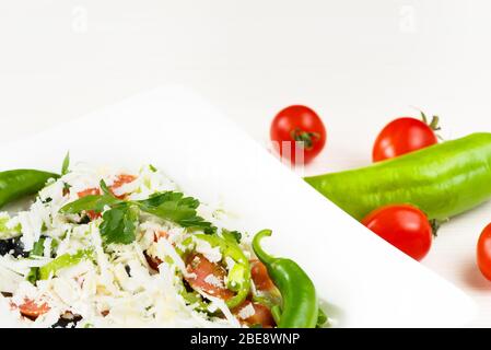 Tradizionale insalata classica Shopska con pomodori, peperoni, cetrioli e formaggio in piatto bianco su tavolo di legno bianco. Cucina bulgara, cultura balcanica Foto Stock