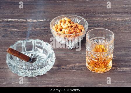 Bicchiere di whisky, sigaro cubano e noci su un tavolo di legno grigio. Vista ravvicinata. Foto Stock