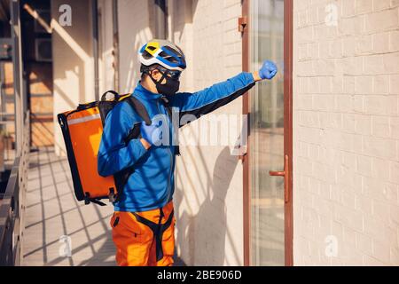 Servizio di consegna senza contatto durante la quarantena. L'uomo consegna cibo e borse per la spesa durante l'isolamento. Bussando alla porta e lascia le merci fino a quando il cliente non la prende. Sicurezza, ricezione, mantenimento della distanza. Foto Stock