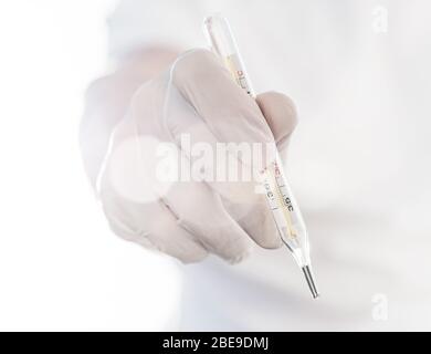 Mano con termometro chirurgico con guanto. Foto Stock