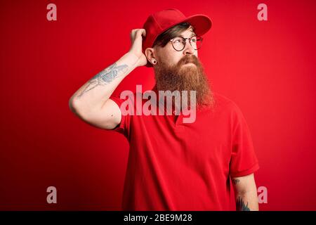 Giovane bel uomo di consegna che indossa occhiali e cappuccio rosso su sfondo isolato confondono e si domanda circa la domanda. Incerto con dubbio, pensando Foto Stock