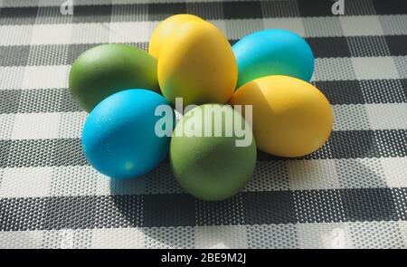 Le uova di Pasqua colorate giacciono su una tovaglia a scacchi. Uova gialle, blu, verdi. Fermo-vita. Foto Stock