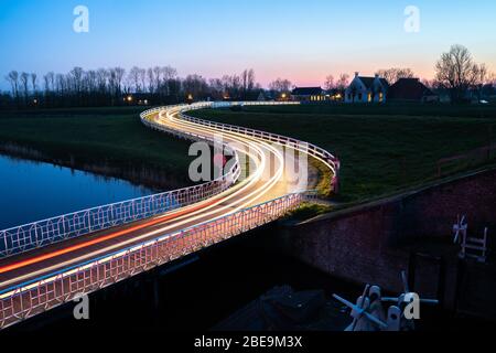 Strada di campagna curva Asphalt nella campagna olandese con recinto bianco che conduce verso un vecchio casale in Olanda. Foto Stock