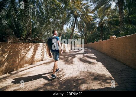 Giovane viaggiatore solista che cammina nel mezzo delle palme. Oasi nel deserto ad al Ain, Emirato Abu Dhabi, Emirati Arabi Uniti Foto Stock