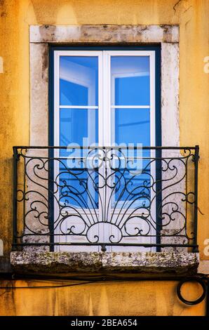 Finestra vecchia e danneggiata con balcone in ferro su una parete gialla Foto Stock