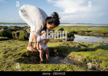 la madre tiene il bambino quando i piedi del bambino sono toccati alla spiaggia di sabbia, godendosi una vacanza alla spiaggia